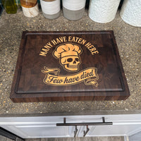 Wooden cutting board with skull design and text on a kitchen counter