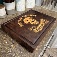 Wooden cutting board with skull design and text on a concrete counter top.