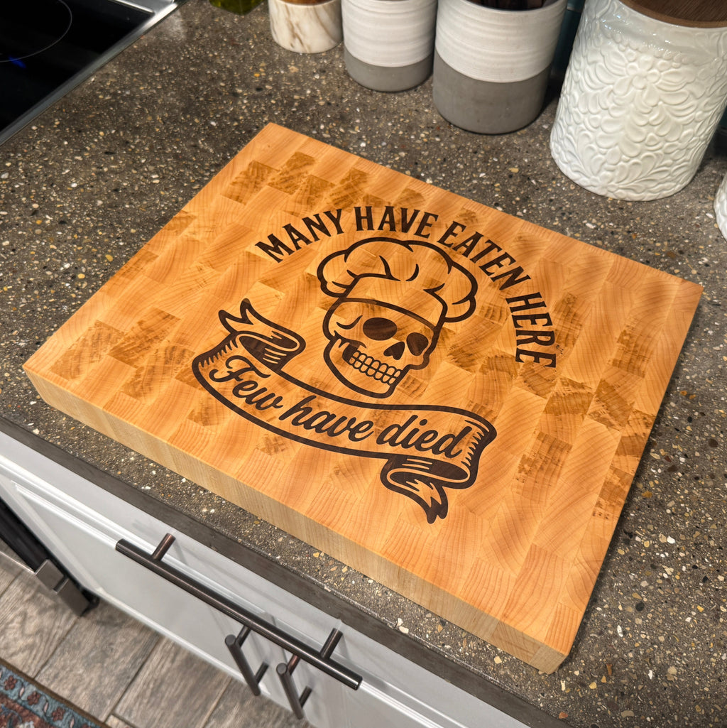 Wooden cutting board with skull and chef hat design on a kitchen counter