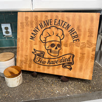Wooden cutting board with skull and chef hat design on a kitchen counter.