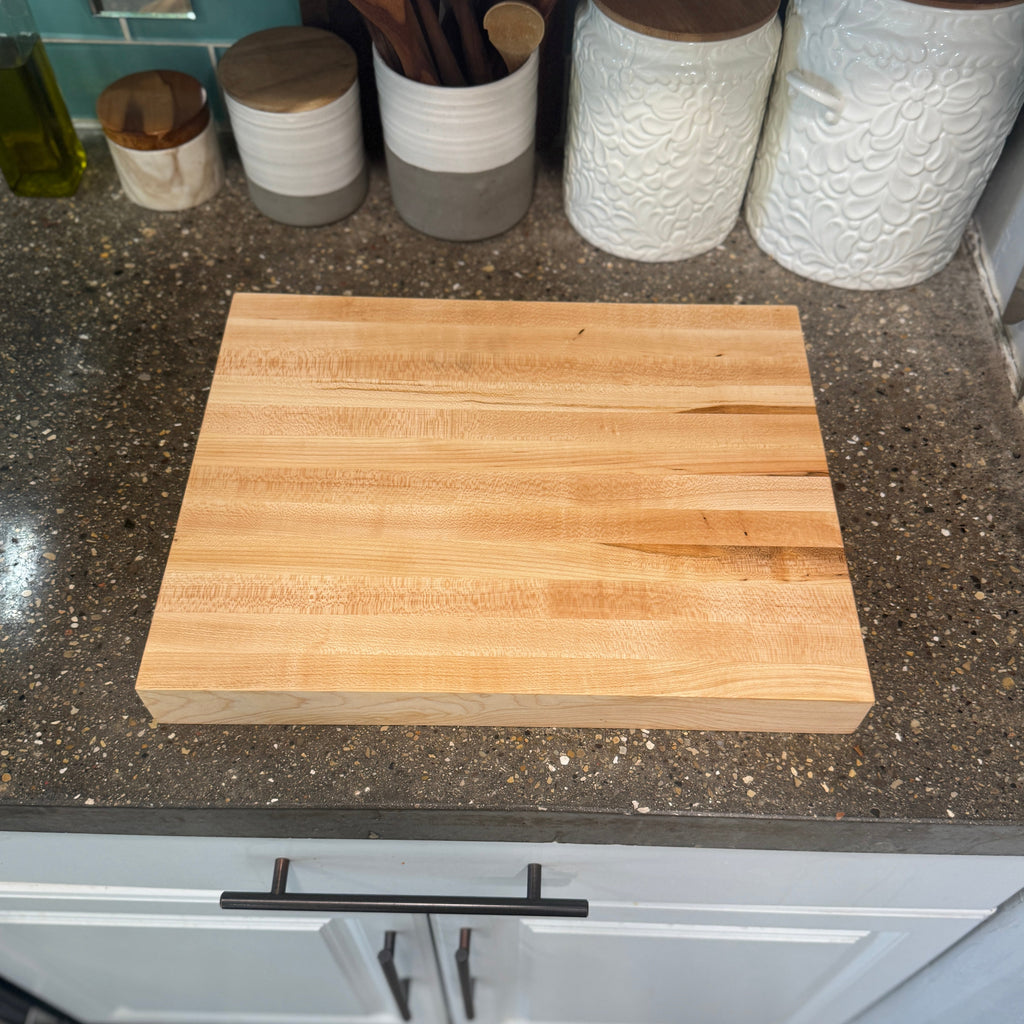 Wooden cutting board on a kitchen counter with storage jars in the background.