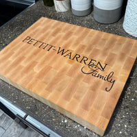 Wooden cutting board with 'PETIT-WARREN Family' engraving on a kitchen counter.